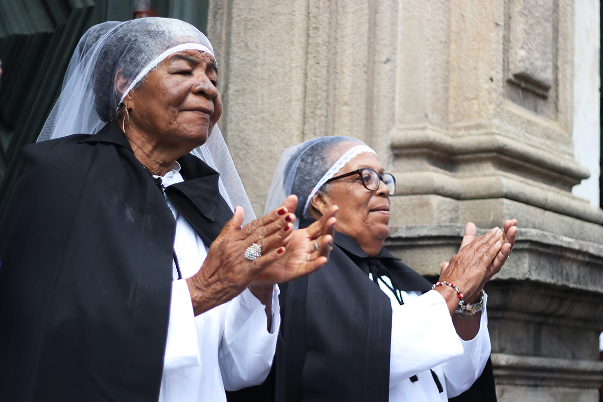 Mulheres que fazem parte da Irmandade dos Homens Pretos batendo palma